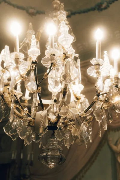 Bridal shoes, white bridal heels gleaming beneath a grand chandelier, their elegant shape highlighted by warm light in a refined venue.