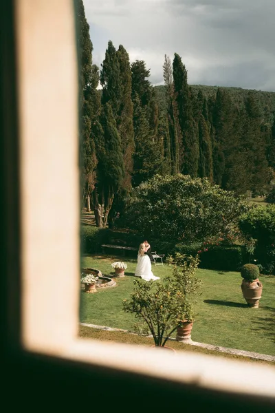 Couple portrait capturing a wedding kiss moment by a garden fountain, framed by cypress trees on the garden lawn.