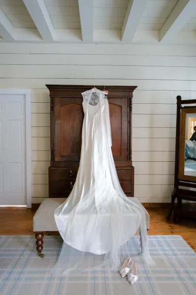 Wedding dress hanging on a wooden hanger with veil draped beside it, set against a shiplap wall in a bridal suite