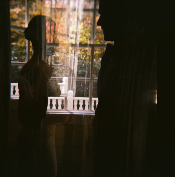Wedding couple portrait of bride and groom silhouette facing each other, veil accent, backlit by large window with autumn balcony foliage