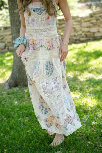 Wedding guest dress with lace maxi dress and multicolor floral print, shown barefoot on a grassy lawn by a stone wall in dappled sun