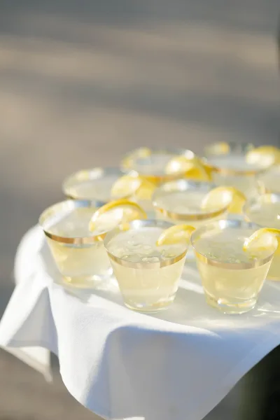 Wedding signature drinks with pale yellow lemonade wedding drink in silver-rim glasses, iced with lemon slices on a white tablecloth in sunlight