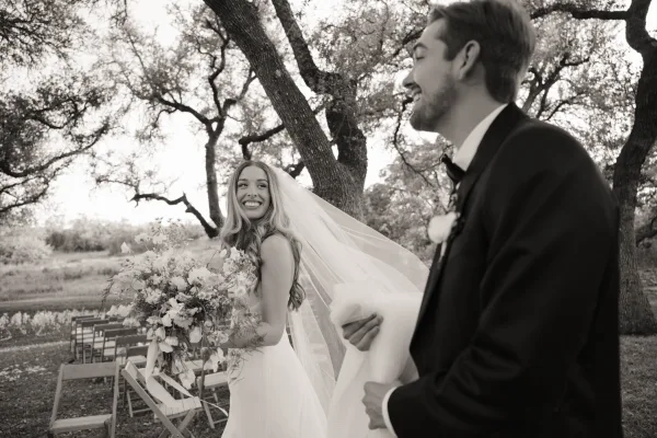 Ceremony moment of bride and groom candid walking down the aisle, bouquet and veil in hand, past ceremony chairs under oak trees