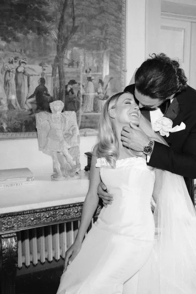 Couple portrait in a black and white wedding portrait, groom kissing bride’s forehead as she laughs in an art-filled interior with veil accent