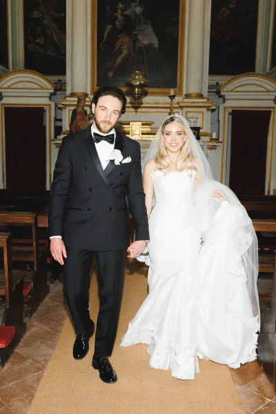 Couple portrait of bride and groom holding hands at a church altar, her long veil and strapless gown beside his black tuxedo