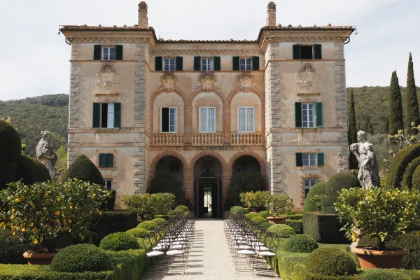 Outdoor ceremony setup with garden ceremony aisle lined by chairs on a gravel path, framed by boxwood hedges and a villa facade backdrop
