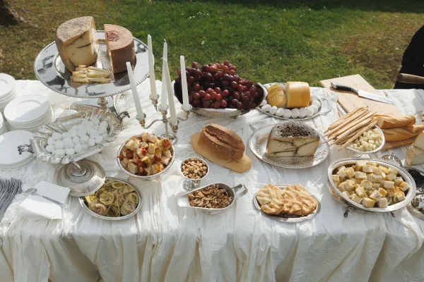 Wedding appetizer table with wedding antipasto spread on silver platters, cheese and bread, grapes and bowls of olives on a lawn outdoors