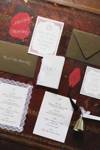 Invitation suite with wedding invitation set in calligraphy, embossed envelope and wax seal, arranged on a distressed vintage wooden table