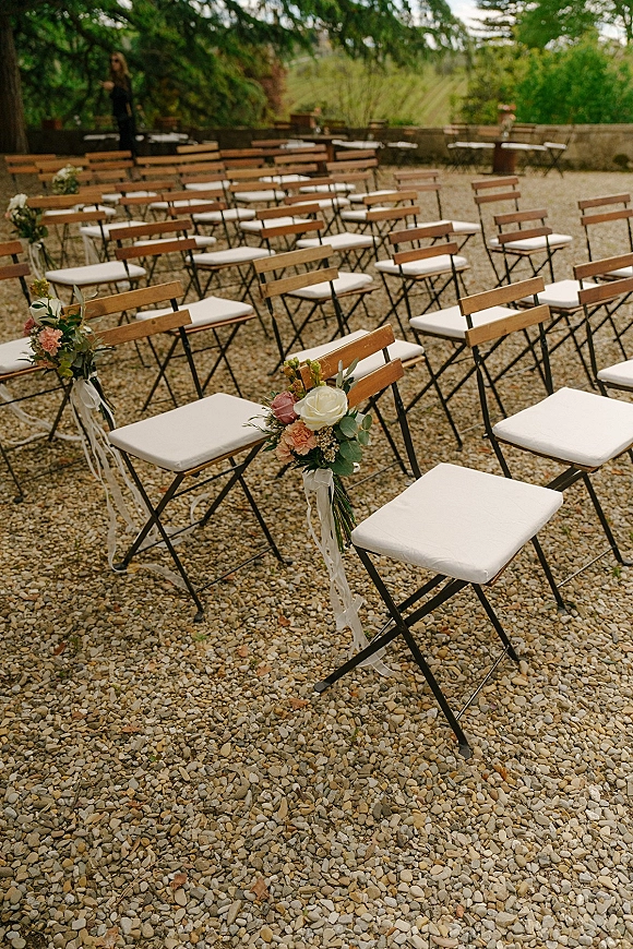 Ceremony seating with outdoor ceremony chairs, wood folding chairs with white cushions and rose greenery aisle florals in a gravel courtyard