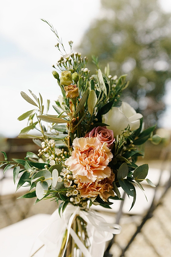 Bridal bouquet with peach bridal bouquet blooms of blush and white roses, waxflower and eucalyptus, tied with white ribbon outdoors near trees