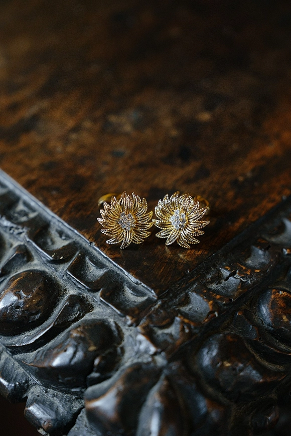 Wedding earrings with diamond cluster centers in gold, resting on a dark wooden surface beside a carved metal box