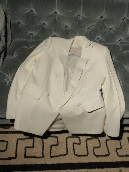 Groom suit with white tuxedo jacket, notched lapel and buttons resting on a tufted velvet sofa over a patterned rug