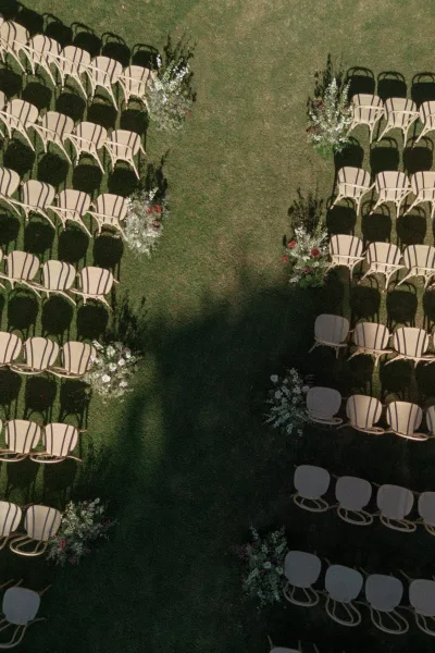 Ceremony seating with curved white chairs and greenery-lined aisle flowers set on a grass lawn for an outdoor garden wedding ceremony