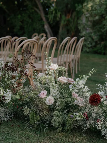 Ceremony aisle decor with outdoor wedding aisle flowers, blush and white ground florals and greenery beside wooden chairs on a garden lawn