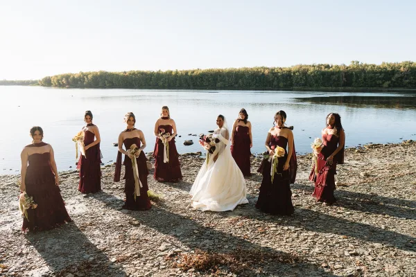Bridal party portrait of bride with bridesmaids holding bouquets, bride in ball gown and veil on a rocky lakeshore by the water