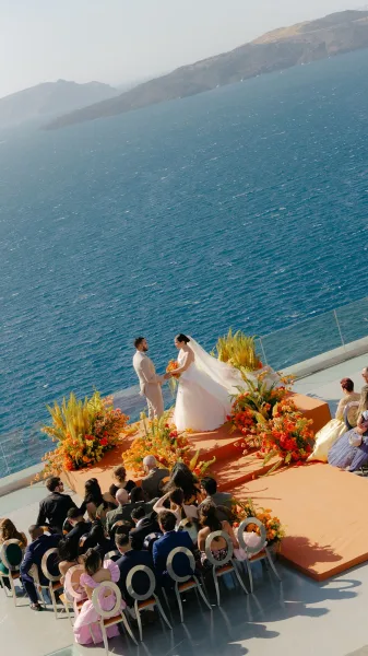 Ceremony moment at an oceanfront ceremony as the couple hold hands on a cliffside terrace, the bride's long veil streaming in the sea breeze.