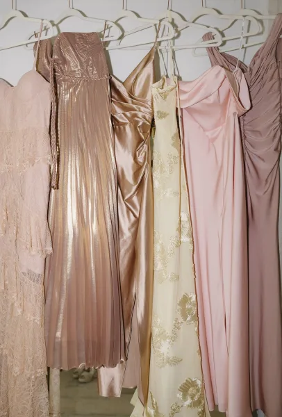 Bridesmaid dresses, including blush bridesmaid dresses, hang neatly on a garment rack, displayed in an organized row.