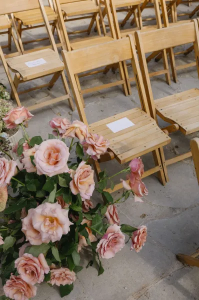 Ceremony aisle decor with an aisle floral arrangement of blush roses marking row ends on a stone patio, creating an elegant, intimate path.