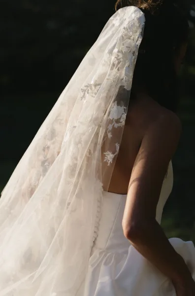 Bridal veil close-up reveals a lace wedding veil with delicate texture, framed by soft garden greenery in the background.