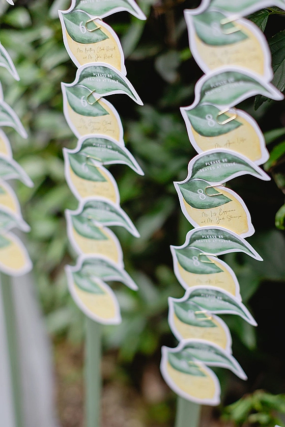 Wedding escort cards with lemon escort cards clipped in gold and hanging on strings, handwritten calligraphy on watercolor paper amid greenery