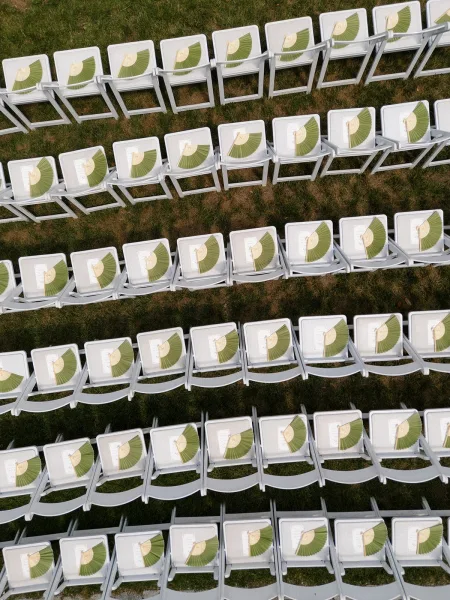 Ceremony seating styled as outdoor ceremony seating on a grass lawn, with paper fans placed on each seat for guest comfort.