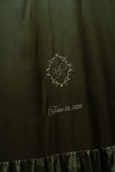 Wedding monogram nestled within a scrollwork crest on dark green fabric, its crisp lettering and balanced layout creating a refined focal point.