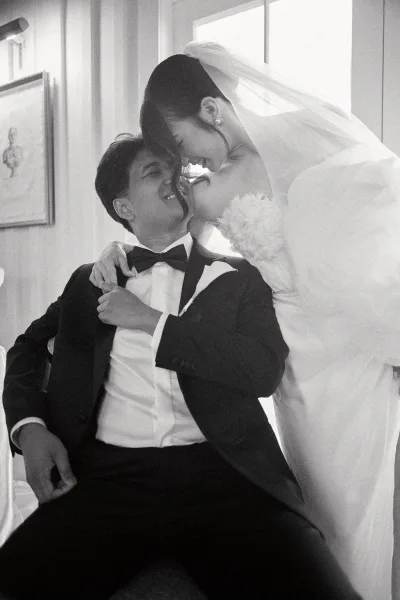 Wedding kiss portrait of a bride kissing her groom as she leans in with a soft bridal veil, the groom smiling by a window with framed artwork.