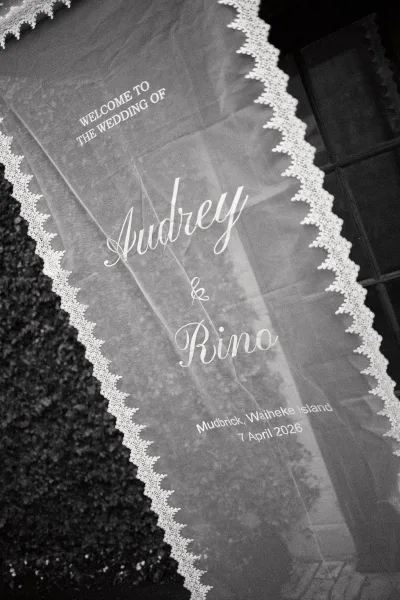 Wedding welcome sign, a fabric wedding sign with lace trim, set against hedge greenery and a window frame in the background.
