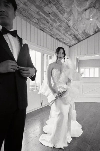 Bridal portrait in black and white, bride holding a calla lily bouquet by French doors with shiplap walls and wood floor.