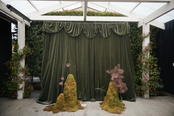 wedding backdrop featuring a green velvet backdrop, draped with moss accents, set against a white pergola and climbing vines