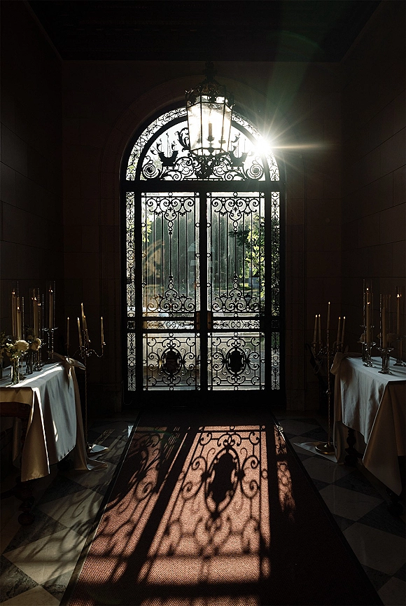 Reception entrance decor with wrought iron wedding doors, candlelit tables and lantern under an arched stone doorway with garden view