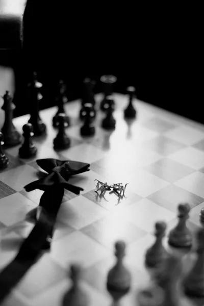 Groom details styled as a bow tie flatlay on a chessboard with scattered chess pieces, highlighting classic black-tie elegance.