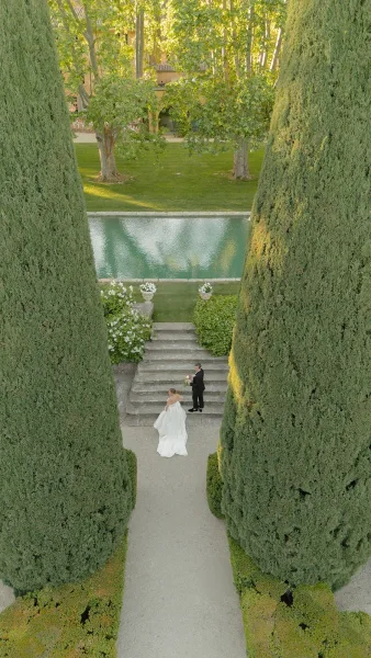 Couple portrait of a bride and groom on steps, her bridal bouquet standing out beside cypress trees and a reflecting pool.