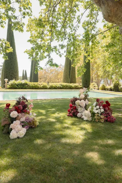Ceremony flowers anchor refined garden ceremony decor with hydrangeas, set as low clusters on a poolside lawn amid cypress trees and hedges.