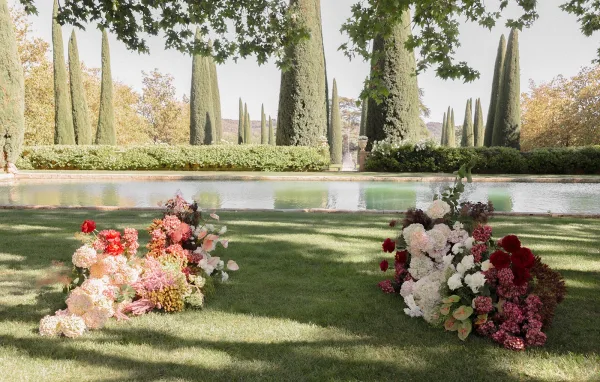 Ceremony aisle design with a grounded floral aisle of hydrangeas beside a reflecting pool framed by tall cypress trees.