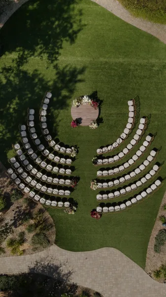 Ceremony setup with outdoor wedding ceremony layout, white chairs curving around a round platform on a garden lawn with floral markers
