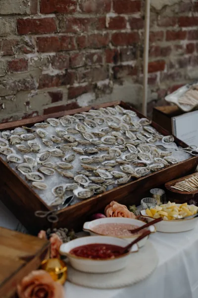 Oyster bar with oysters on ice, lemon wedges, sauces, and wooden trays on a buffet table against a brick wall backdrop