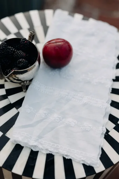 Wedding tablescape with a black and white table setting, embroidered white napkin and vintage silver bowl of blackberries and plum by brick wall