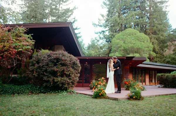 Wedding kiss as bride and groom kissing on a stone patio, bride in veil and strapless dress, modern house windows behind