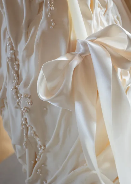 Wedding dress detail highlighting a satin bow that cinches the bodice, set against ivory fabric with soft shadows for a refined, romantic look.