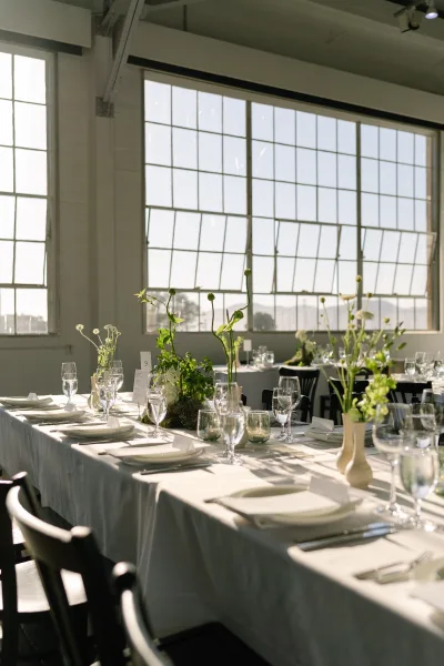 Reception tablescape for indoor reception decor featuring bud vases, set by large windows with black chairs and a city view.