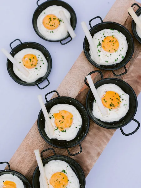Wedding appetizers styled as cocktail hour bites, served in mini skillets and arranged on a wooden serving board for individual portions.