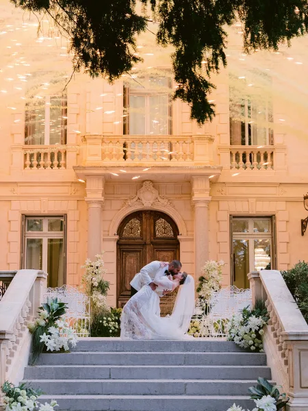 Wedding kiss portrait capturing a dip kiss wedding photo on stone steps by carved mansion doors, the bride in a lace bridal gown.