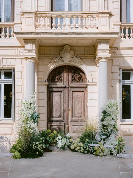 Ceremony setup with outdoor ceremony decor before a stone facade with wooden double doors, featuring wrought iron chairs in the courtyard.