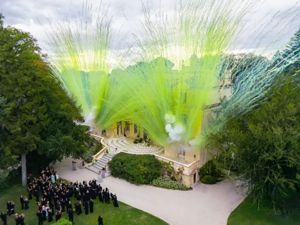 Wedding fireworks flare in a daytime wedding fireworks display above a stone staircase, set before the mansion exterior under a cloudy sky.