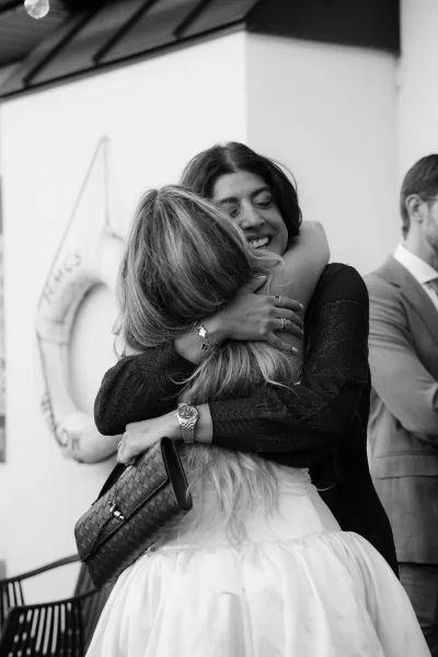Wedding hug as the bride hugs a guest, a clutch bag tucked under her arm, with a bright lifebuoy behind them.