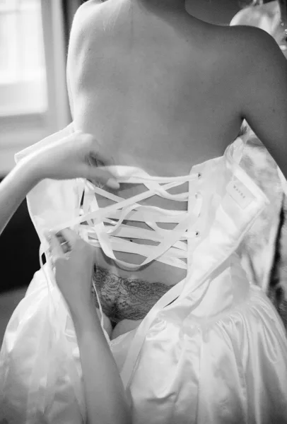 Bride getting ready, getting into wedding dress as corset lacing is threaded and tightened at the back, close-up detail.