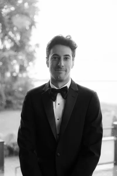 groom portrait of a black tie groom with a black bow tie by a window overlooking garden trees and a calm water view