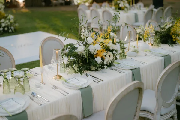 Reception tablescape on an outdoor wedding table with green glass goblets beside a white dance floor.