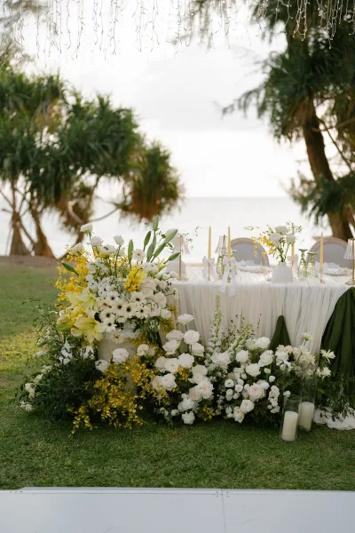 Sweetheart table decor in a coastal reception decor setting, accented by taper candles, set on a grass lawn overlooking the ocean.